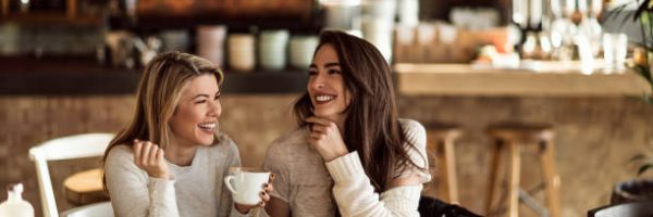 Young happy women talking and laughing while drinking coffee together in coffee shop.
