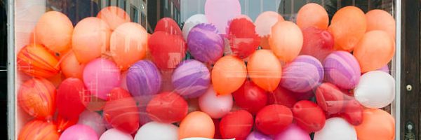Colorful balloons fill storefront window. Horizontal.